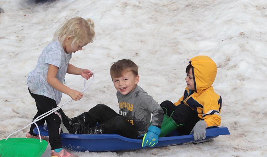 Three kids sliding down the snow hill