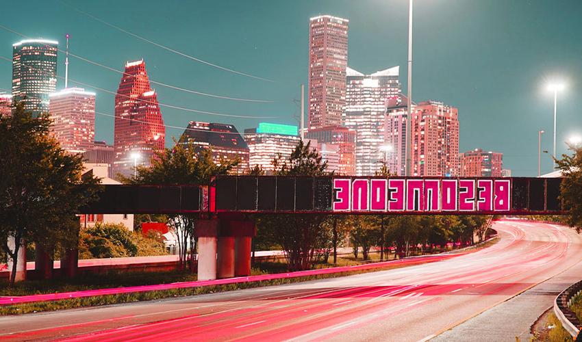 Pictures of "Be Someone" painting at night with lit Houston buildings in the back.